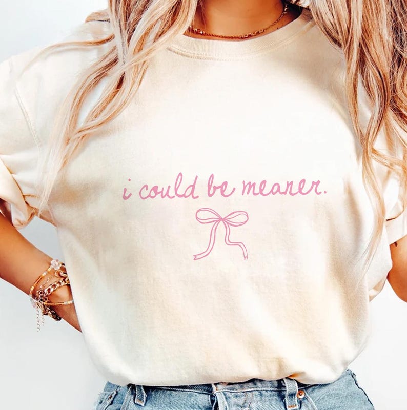 May include: Cream-colored sweatshirt with the phrase "i could be meaner" in pink script above a pink bow graphic. The long-sleeved shirt is made of a soft material.