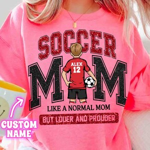 May include: Pink sweatshirt with the words "SOCCER MOM" in glittery red letters. The letter "M" is in black with a white outline. A graphic of a soccer player is in the center. The text "LIKE A NORMAL MOM BUT LOUDER AND PROUDER" is below.
