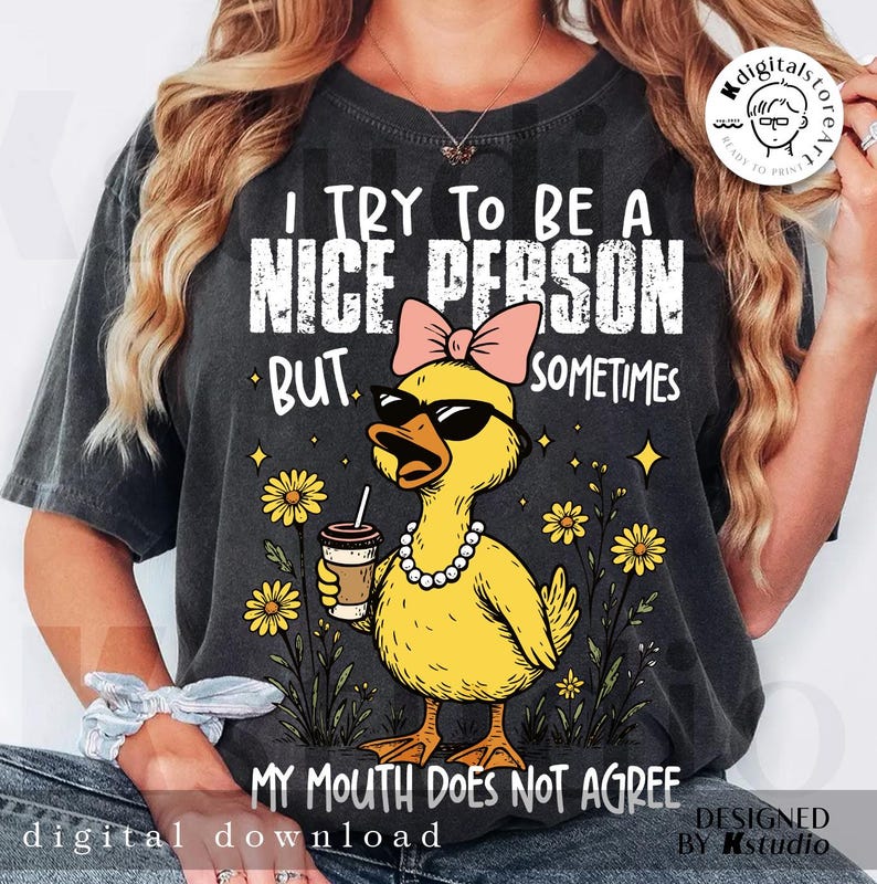 May include: Dark grey t-shirt featuring a yellow duck wearing sunglasses and a pink bow, holding a coffee cup. Text reads "I TRY TO BE A NICE PERSON BUT SOMETIMES MY MOUTH DOES NOT AGREE." The design includes daisies and stars.