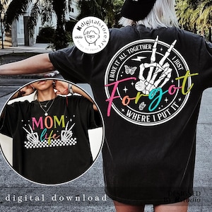 May include: Two black t-shirts with colorful graphic designs. One shirt features the text "Mom Life" with a checkered background and two skeleton hands making the peace sign. The other shirt features a skeleton hand with the text "I Have It All Together I Just Forgot Where I Put It".