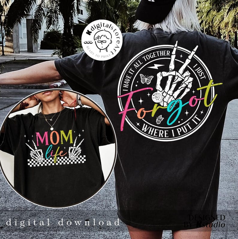 May include: Two black t-shirts with colorful graphic designs. One shirt features the text "Mom Life" with a checkered background and two skeleton hands making the peace sign. The other shirt features a skeleton hand with the text "I Have It All Together I Just Forgot Where I Put It".