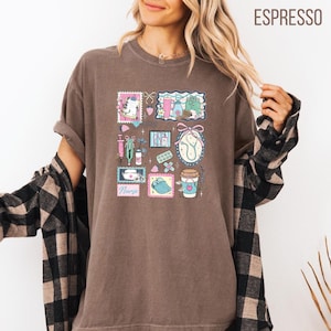 Op de afbeelding: Bruin T-shirt met een medisch thema collage ontwerp. Het ontwerp bevat een spuit, stethoscoop, pillen en een koffiekopje met een hart. Het woord "Nurse" is ook zichtbaar in het ontwerp.