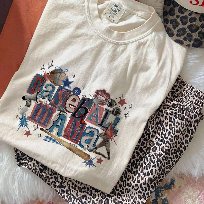 K&ouml;nnte beinhalten: Cremefarbenes T-Shirt mit dem Schriftzug "Baseball Mama" in einem farbenfrohen Grafikdesign. Das Shirt wird mit einer Hose mit Leopardenmuster und einer Baseballkappe mit Leopardenmuster kombiniert.