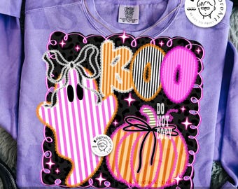 May include: A lavender Comfort Colors sweatshirt with a Halloween-themed graphic. The graphic features a ghost, pumpkin, and the word "BOO" in a playful font. The design includes black, white, pink, and orange colors.