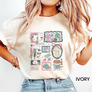 Op de afbeelding: Ivoor kleurig T-shirt met een collage van medische postzegelontwerpen. De postzegels bevatten een stethoscoop, een spuit, pillen en een koffiekopje. Het woord "Nurse" staat op een postzegel. Het shirt is gemaakt van een zacht materiaal.