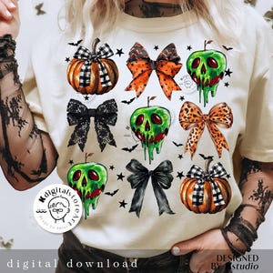May include: Cream-colored t-shirt featuring Halloween-themed graphics. The design includes pumpkins, bows, and green apple skulls. The words "digital download" and "designed by studio" are printed on the shirt.