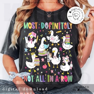 May include: Dark gray t-shirt with a colorful graphic featuring cartoon ducks with books, pencils, and the text "MOST DEFINITOLY NOT ALL IN A ROW." The design includes stars and flowers.
