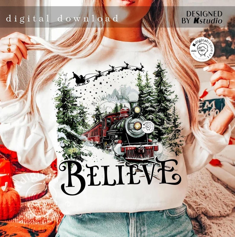 May include: White sweatshirt with a Christmas-themed design featuring a red train traveling through a snowy forest with a red sleigh and reindeer flying above. The text "BELIEVE" is printed below the train.