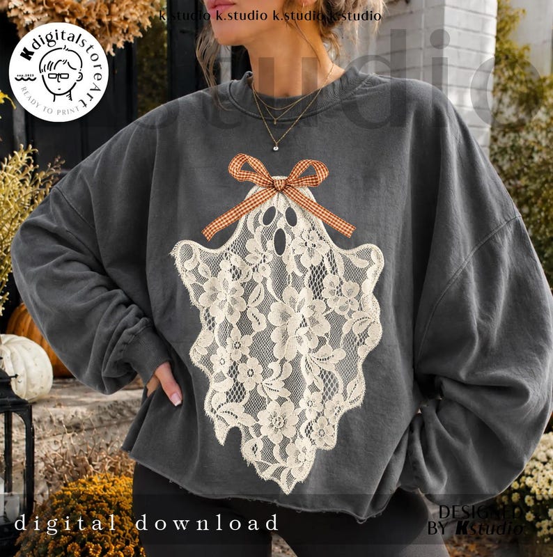 May include: A charcoal gray crewneck sweatshirt featuring a large, off-white lace ghost graphic on the front. The ghost design is adorned with a small, orange and white checkered gingham bow at the top, creating a textured, layered appearance.