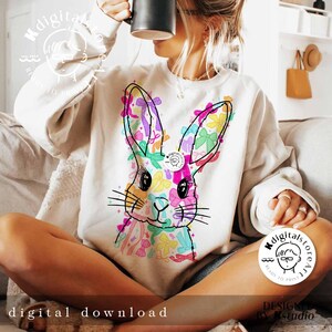 May include: A white sweatshirt with a colorful graphic of a bunny rabbit with bows. The bunny is surrounded by colorful bows and flowers. The text "digitalstoreatl" is on the bottom right corner of the sweatshirt.