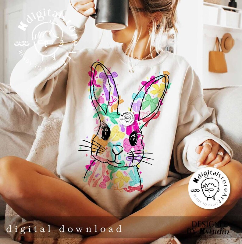 May include: A white sweatshirt with a colorful graphic of a bunny rabbit with bows. The bunny is surrounded by colorful bows and flowers. The text "digitalstoreatl" is on the bottom right corner of the sweatshirt.