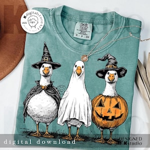 May include: A teal Comfort Colors t-shirt featuring a Halloween-themed design. The graphic depicts three geese dressed as a witch, a ghost, and a jack-o'-lantern. The words "digital download" are printed at the bottom. A silver necklace is draped across the shirt.