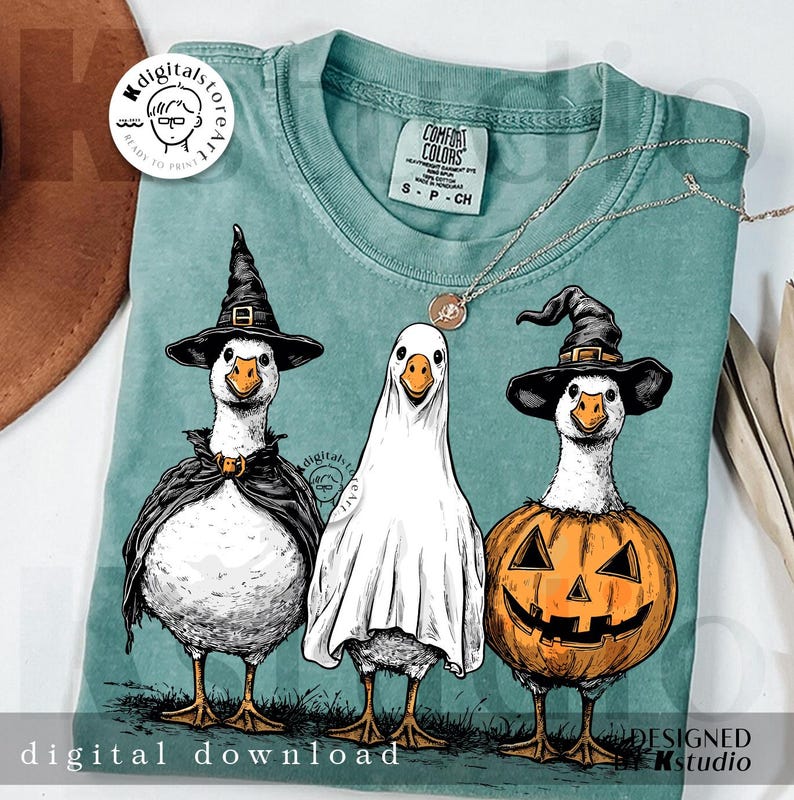 May include: A teal Comfort Colors t-shirt featuring a Halloween-themed design. The graphic depicts three geese dressed as a witch, a ghost, and a jack-o'-lantern. The words "digital download" are printed at the bottom. A silver necklace is draped across the shirt.