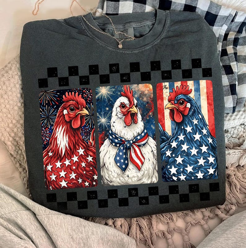 May include: Dark gray sweatshirt featuring three chickens with patriotic designs. One chicken is red with white stars, another is white with a patriotic scarf, and the last is blue with white stars. A black and white checkered pattern is above the chickens.
