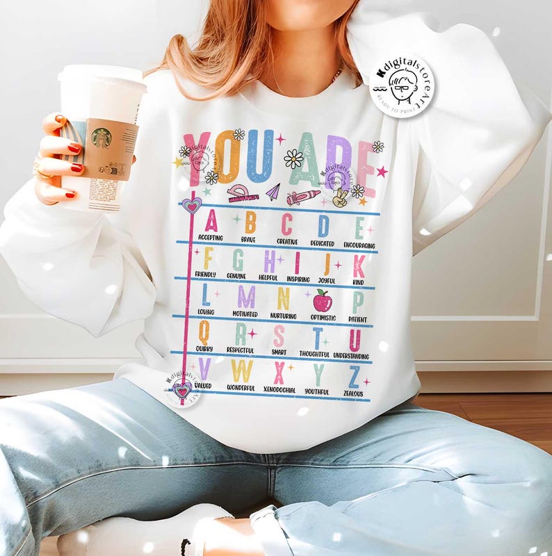 May include: White sweatshirt with a colorful alphabet chart that says "You Are" at the top. Each letter of the alphabet is paired with a positive adjective. For example, "A" is for "Accepting" and "B" is for "Brave".