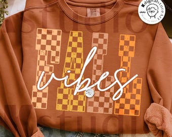 May include: A brown sweatshirt with the words "FALL VIBES" in white script. The letters "FALL" are designed with a checkered pattern in shades of orange and brown. The sweatshirt is a digital download.