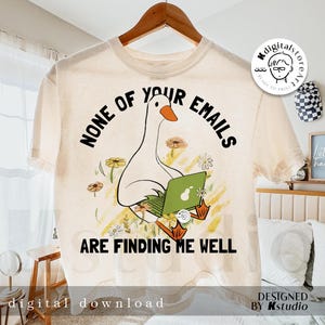 以下が含まれることがあります： ノートパソコンを使用している漫画のガチョウが描かれたクリーム色のTシャツ。周りには花が描かれています。「NONE OF YOUR EMAILS ARE FINDING ME WELL」の文字がガチョウの上と下にプリントされています。木製のハンガーにシャツが掛かっています。