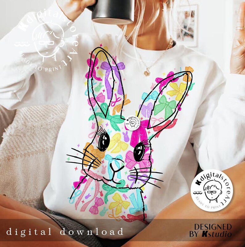 May include: A white sweatshirt with a colorful graphic of a bunny rabbit made of bows. The bunny is surrounded by a variety of colorful bows in pink, blue, yellow, green, and purple.