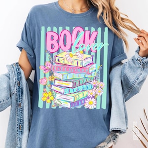May include: Blue t-shirt with a graphic of a stack of books, flowers, and the words "BOOK Lover" in pink and teal. The books are in various colors, and the flowers are pink and yellow.