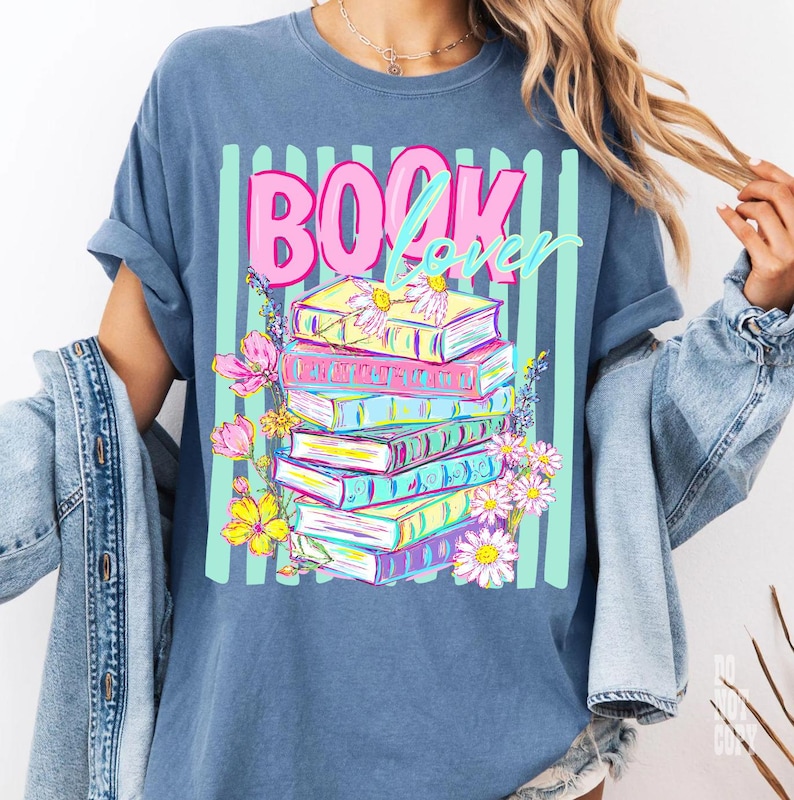 May include: Blue t-shirt with a graphic of a stack of books, flowers, and the words "BOOK Lover" in pink and teal. The books are in various colors, and the flowers are pink and yellow.