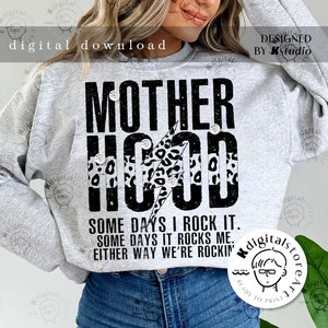 May include: A gray sweatshirt with the text "MOTHERHOOD" in black with a black lightning bolt and leopard print design. The text "SOME DAYS I ROCK IT. SOME DAYS IT ROCKS ME. EITHER WAY WE'RE ROCKIN'" is printed below the main text.
