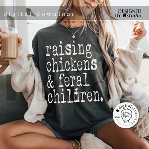 May include: A dark gray t-shirt with the text "raising chickens & feral children." printed in white.