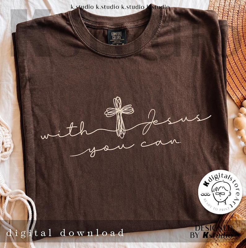Op de afbeelding: Een donkerbruin T-shirt met korte mouwen en een witte lijntekening van een kruis. De tekst "with Jesus you can." staat in cursief schrift op de borst. Het shirt heeft een ronde hals en een Comfort Colors merklabel.