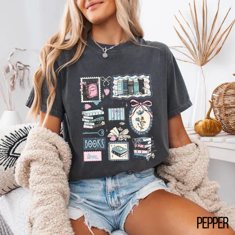 May include: Dark gray t-shirt featuring a collection of book-themed illustrations. The design includes stacks of books, floral elements, and the word "BOOKS" with "love" underneath. The shirt is a comfortable, casual style.