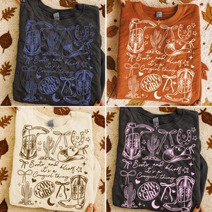 May include: Four crew neck sweatshirts in different colors: charcoal, rust, cream, and dark grey. Each shirt features a western-themed graphic with boots, a cowboy hat, and the text "Boots and Bling, it's a Cowgirl thing."