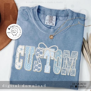 May include: A light blue t-shirt with the word "CUSTOM" in a decorative font. The letters are embellished with seashells, pearls, and other nautical designs. A gold necklace with a pendant is draped across the shirt. The words "digital download" are at the bottom.
