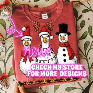May include: Red sweatshirt featuring three geese dressed for Christmas. One goose wears a Santa hat, another has antlers and lights, and the third is a snowman. The text "NEW" and "CHECK MY STORE FOR MORE DESIGNS" are also visible.