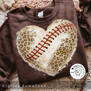 Op de afbeelding: Een bruine sweatshirt met een honkbal-thema hart ontwerp. Het hart combineert een luipaardprint met een honkbalsteekpatroon. De woorden "digital download" staan onderaan afgedrukt.