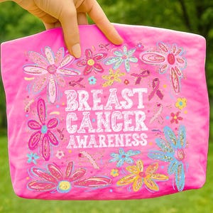 May include: A pink tote bag with the words "BREAST CANCER AWARENESS" in white, surrounded by colorful flowers and pink ribbons. The flowers have blue, yellow, and pink accents.