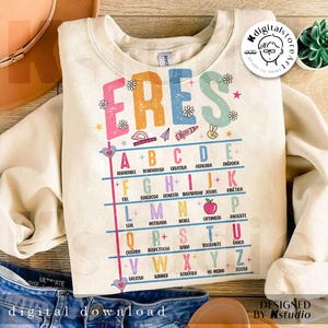 May include: Cream-colored sweatshirt with the word "ERES" in colorful letters. Below, an alphabet chart with positive adjectives in Spanish. The design includes hearts, flowers, and school-themed illustrations.