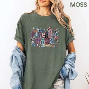 K&ouml;nnte beinhalten: Olivgr&uuml;nes T-Shirt mit dem Text "Baseball Mama" in einem farbenfrohen Grafikdesign. Das Design enth&auml;lt Baseball-Elemente wie einen Baseballschl&auml;ger, Sterne und einen Baseball. Das Shirt hat hochgekrempelte &Auml;rmel und eine lockere Passform.
