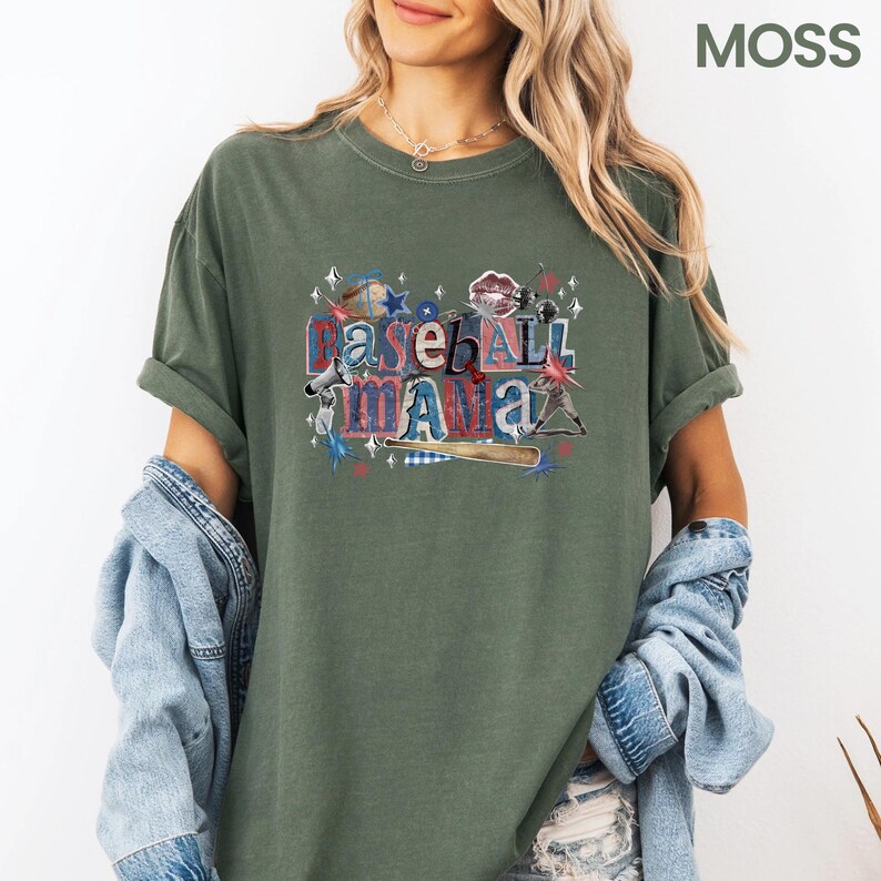 K&ouml;nnte beinhalten: Olivgr&uuml;nes T-Shirt mit dem Text "Baseball Mama" in einem farbenfrohen Grafikdesign. Das Design enth&auml;lt Baseball-Elemente wie einen Baseballschl&auml;ger, Sterne und einen Baseball. Das Shirt hat hochgekrempelte &Auml;rmel und eine lockere Passform.