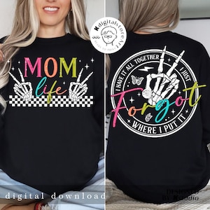 May include: A black t-shirt with a colorful graphic on the front that says "MOM life" with two skeleton hands making the peace sign. The back of the shirt has a white circle with the text "I have it all together I just forgot where I put it" with a skeleton hand making the peace sign.