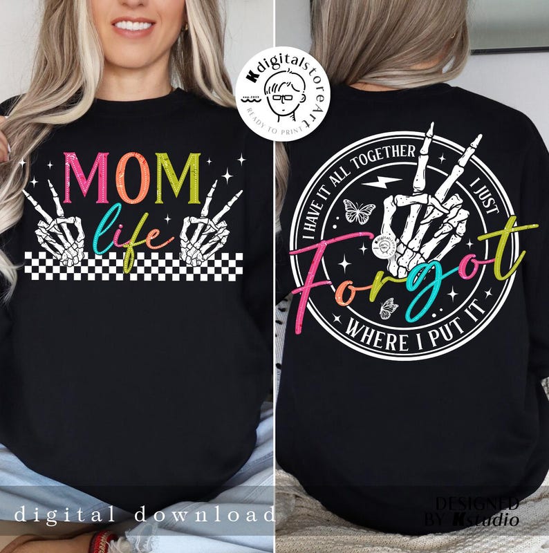 May include: A black t-shirt with a colorful graphic on the front that says "MOM life" with two skeleton hands making the peace sign. The back of the shirt has a white circle with the text "I have it all together I just forgot where I put it" with a skeleton hand making the peace sign.