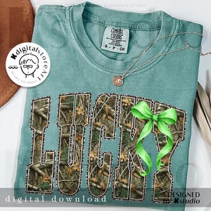 May include: A teal Comfort Colors t-shirt with the word "LUCKY" in a camouflage pattern. A green bow is attached to the letter "Y". A silver necklace with a pendant is also visible. The words "digital download" and "designed by kstudio" are also visible.
