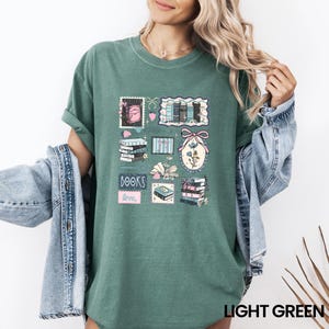 May include: Light green t-shirt featuring a collage of book-themed illustrations. The design includes stacks of books, floral elements, and the words "BOOKS" and "love". The shirt is a solid light green color.