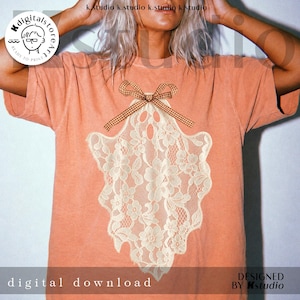 May include: A peach-colored short-sleeve t-shirt featuring a central graphic of a ghost shape composed of cream-colored floral lace. The ghost design is accented at the top with a brown and white gingham patterned bow graphic.