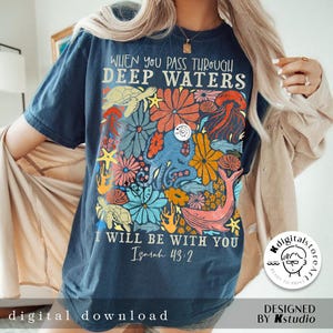 May include: A navy blue t-shirt with a colorful floral design featuring sea creatures like an octopus, turtle, and whale. The text "When you pass through deep waters I will be with you Isaiah 43:2" is printed on the shirt.
