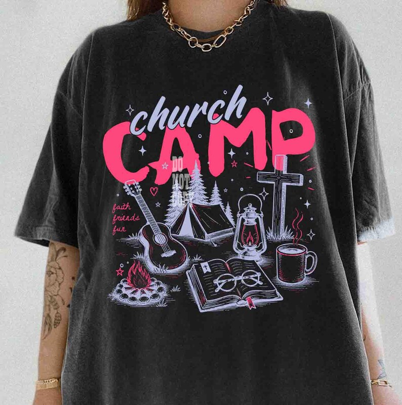 K&ouml;nnte beinhalten: Schwarzes T-Shirt mit einem Grafikdesign mit den Worten "church CAMP" in Pink, zusammen mit Illustrationen einer Gitarre, eines Zeltes, eines Kreuzes, einer Laterne, eines Lagerfeuers, eines Buches und einer Kaffeetasse. Die Worte "faith friends fun" sind ebenfalls enthalten.