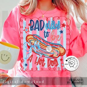 May include: Pink sweatshirt with the text "BAD day to be A Hot Dog" and a graphic of a hot dog. The design includes red, white, and blue stars and stripes. The words "digital download" are at the bottom.