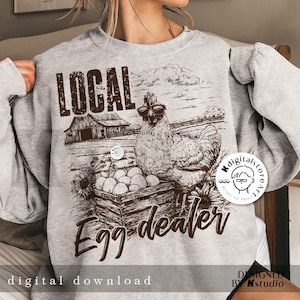 May include: A gray sweatshirt with a brown graphic of a chicken wearing sunglasses and a basket of eggs. The text "LOCAL Egg-dealer" is printed on the sweatshirt.