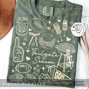 May include: Green t-shirt with white illustrations of tailgate-themed items, including a beer can, football, burger, grill, and the text "Tailgate Season." The shirt also has the text "digital download" and "designed by kstudio."