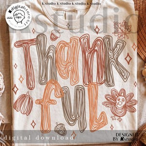 K&ouml;nnte beinhalten: Ein cremefarbenes T-Shirt mit dem Wort THANKFUL in einem braun-orangen Linien-Stil. Das Design enth&auml;lt Illustrationen einer Eichel, eines K&uuml;rbisses, eines Truthahns, eines Ahornblatts und kleiner vierzackiger Sterne, die um den Text verteilt sind.