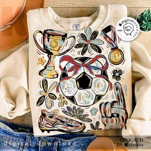 K&ouml;nnte beinhalten: Cremefarbenes Sweatshirt mit Fu&szlig;ballmotiv. Das Design umfasst einen Fu&szlig;ball mit roter und blauer Schleife, eine Troph&auml;e, eine Medaille, einen Fu&szlig;ballschuh und einen Schaumstoff-Finger. Die Worte "digitaler Download" stehen unten.