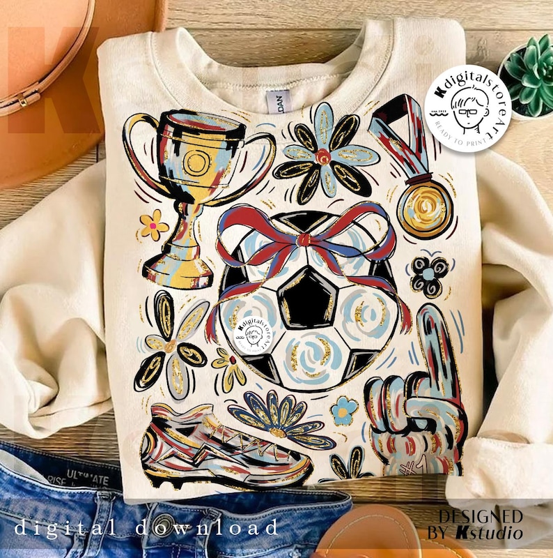 K&ouml;nnte beinhalten: Cremefarbenes Sweatshirt mit Fu&szlig;ballmotiv. Das Design umfasst einen Fu&szlig;ball mit roter und blauer Schleife, eine Troph&auml;e, eine Medaille, einen Fu&szlig;ballschuh und einen Schaumstoff-Finger. Die Worte "digitaler Download" stehen unten.