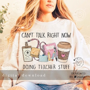 May include: White sweatshirt with the text "CAN'T TALK RIGHT NOW DOING TEACHER STUFF." The graphic includes a coffee cup, notepad, ID badge, sticky notes, and pencils. The words "digital download" are also visible.